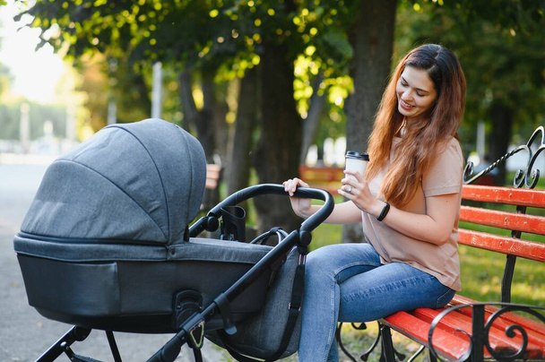 Mum sitting on a bench. Woman pushing her toddler sitting in a pram. Family concept. - Photo, Image