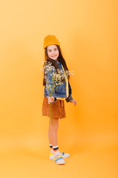 Χαριτωμένο κοριτσάκι φορώντας φωτεινά κομψά ρούχα σε ένα κίτρινο πολύχρωμο φόντο - Φωτογραφία, εικόνα