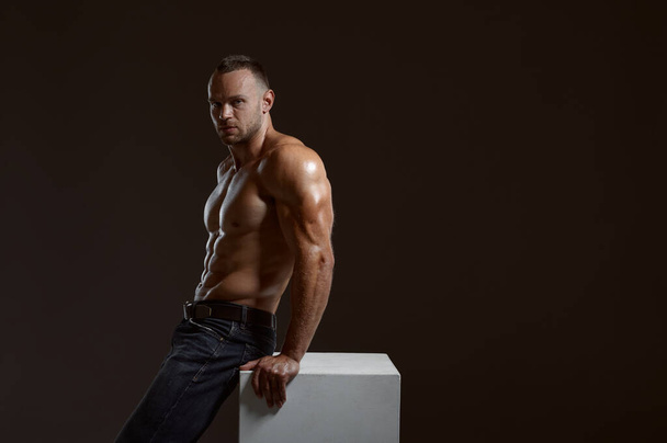 Male muscular athlete sitting on cube in studio - Photo, Image