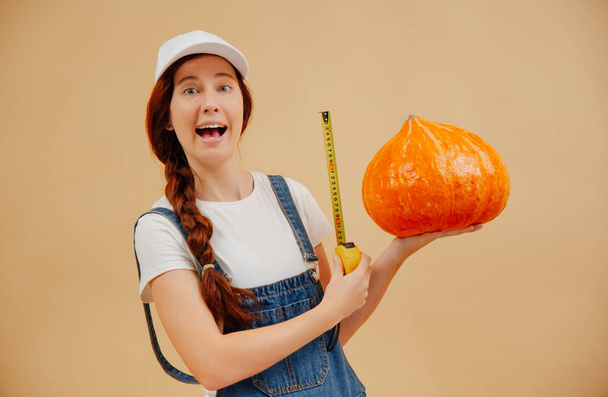 Farmer woman measures large size of pumpkin harvest with tape measure. - Foto, Bild