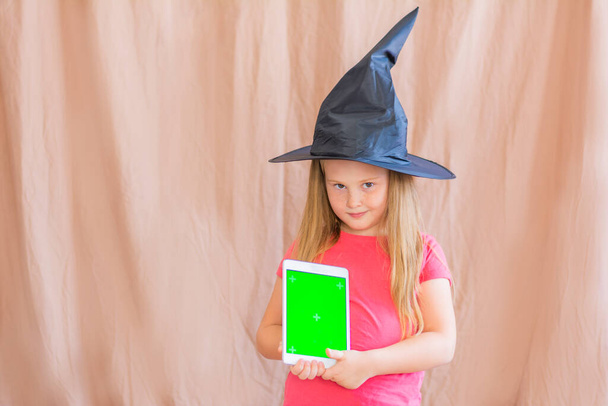 Portrait of a girl in a witch hat with a green mockup tablet screen halloween copy space - Foto, immagini