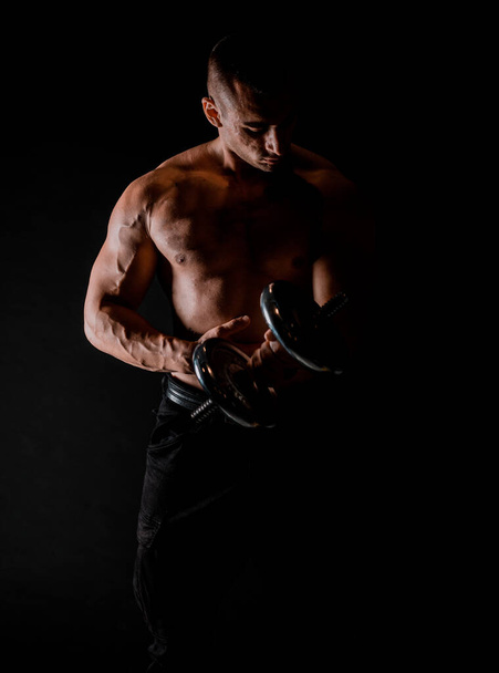 Мускулистый бодибилдер делает упражнения с гантелями на черном фоне - Фото, изображение