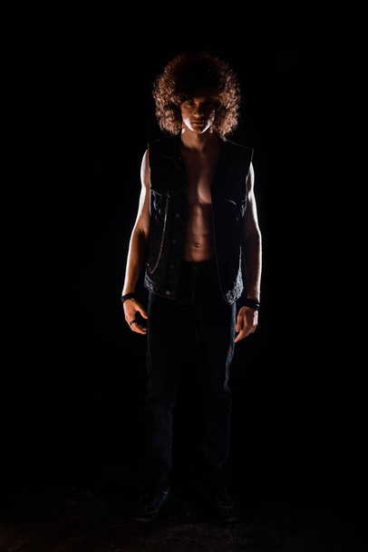 Cooler junger Mann in schwarzer Jeansweste, schwarzer Jeans und Turnschuhen posiert - Foto, Bild