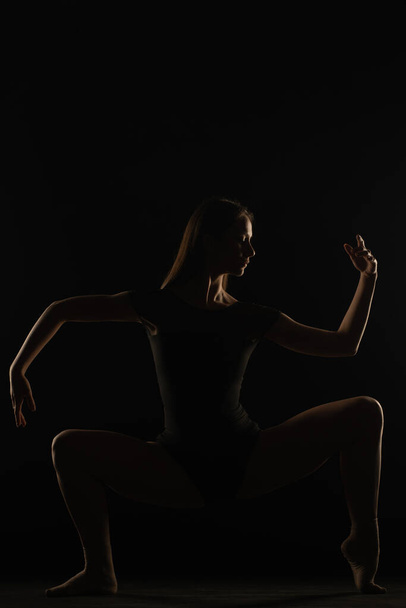 Female ballerina silhouette is doing a asymmetrical pose in studio - Photo, Image
