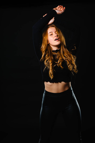 Portrait of a beautiful young adult sensuality woman wearning black tank top and latex pants isolated on dark background - Photo, Image
