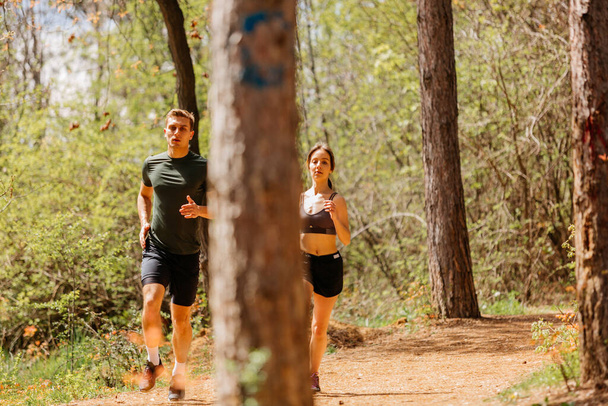 Man en vrouw samen aan het trainen en joggen in het park. Gelukkig en glimlachend als ze op een warme zomerdag langs het pad rennen tijdens zonsondergang - Foto, afbeelding