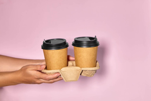 Großaufnahme auf rosa Hintergrund, die Hand einer Frau hält eine Papptasse mit Kaffee in einem Ständer. Kaffee oder Tee to go. Menschen reichen einander Tasse Kaffee, Kaffee-Lieferung. - Foto, Bild