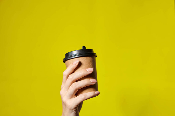 Hands holding two cups brown paper with black lid. Two coffee special offer or promo. Hands holding two cups on yellow screen background. Tea or Coffee to go. Brown paper cup with black lid. - Foto, afbeelding