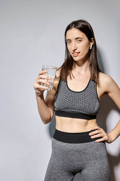 Женщина в спортивной одежде и с беспроводными наушниками пьет воду. концепция здорового образа жизни и спортивных мероприятий - Фото, изображение