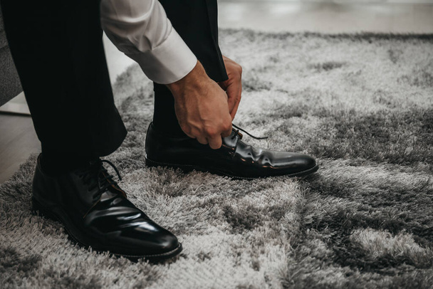 Closeup view of groom's hands lacing classic black shoes. - Photo, Image