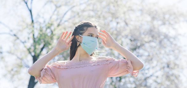 A young female in a medical face mask to avoid the spread coronavirus between flowering trees. - Photo, Image