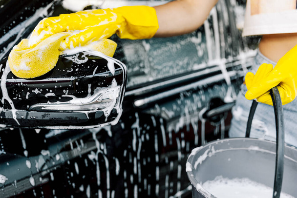 A woman's hand with a yellow sponge for washing, washing a car. - 写真・画像