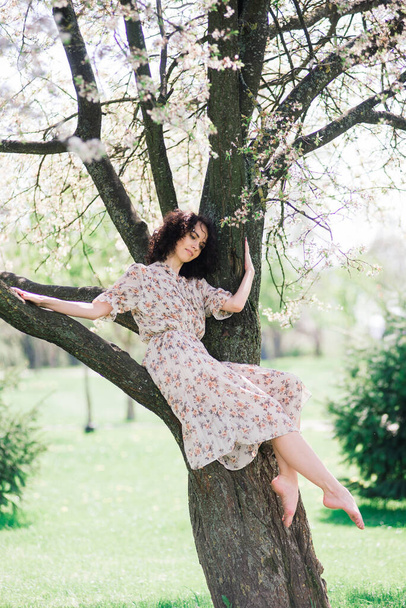 Bahar çiçekli bahçede poz veren kıvırcık saçlı çekici bir kadın. - Fotoğraf, Görsel