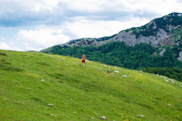 Guy Tourist geht auf einem grünen Hügel spazieren. Durmitor National Park. Höchster Straßenpass in Montenegro, im Norden Montenegros gelegen. Bewölkte Sommerlandschaft. - Foto, Bild