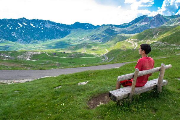 デュルモーター国立公園の山々や道路、モンテネグロで最も高い道路のパスの背景にある緑の丘の上の木製の丘の上に観光客の男。美しい夏の曇りの風景. - 写真・画像