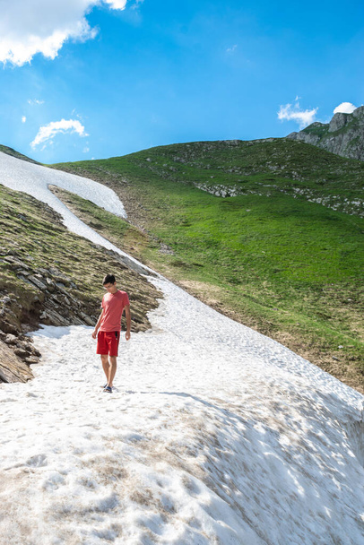 Ein Tourist spaziert im Schnee, der an einem Berghang in der Nähe einer Hochgebirgsstraße liegt, dem höchsten Straßenpass Montenegros. Durmitor National Park. Sommer sonnige grüne Landschaft. - Foto, Bild