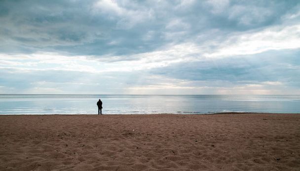 Una persona parada en la playa rodeada por el mar bajo un cielo nublado - Foto, Imagen