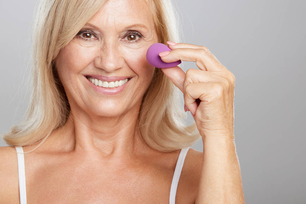 Beautiful senior woman blending her make-up with beauty sponge. Beauty photography - Foto, afbeelding