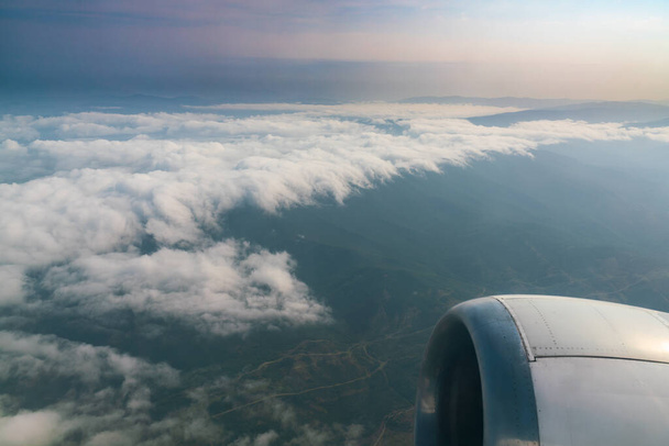 Blick auf die Wolken am Himmel vor dem Flugzeugfenster, während man hoch über dem Boden fliegt - Foto, Bild