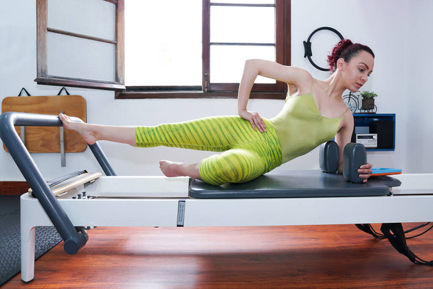 Jeune femme latine faisant des exercices d'étirement sur pilates machine - Photo, image