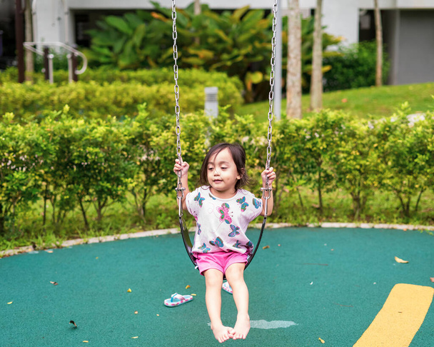 Image floue de mignon petit enfant souriant tout en jouant swing par elle-même à l'aire de jeux de l'enfant, vue de l'enfant flou assis sur balançoire seul. - Photo, image