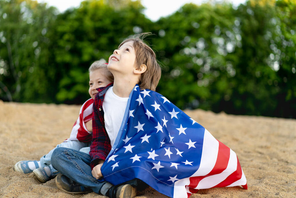 brother and sister on the shore, wrapped in an American flag, happy laughing children, a girl and a boy, the concept of patriotism and the celebration of US independence. US Veterans Day. - Photo, Image