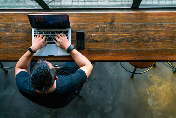 Young Asian businessman using laptop on wooden table - 写真・画像