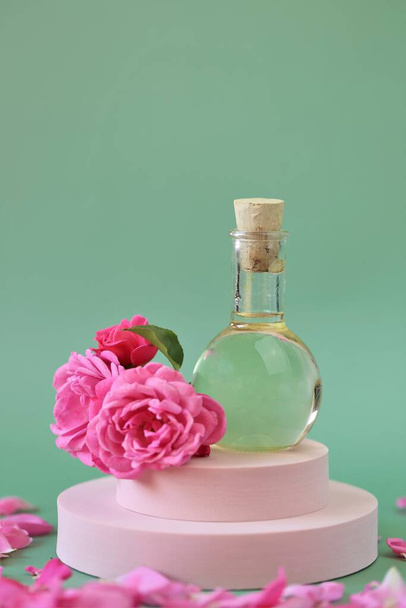 Essential rose oil. Aromatherapy and massage.Rose oil and pink roses set on a pink podium on light green background. - Fotoğraf, Görsel