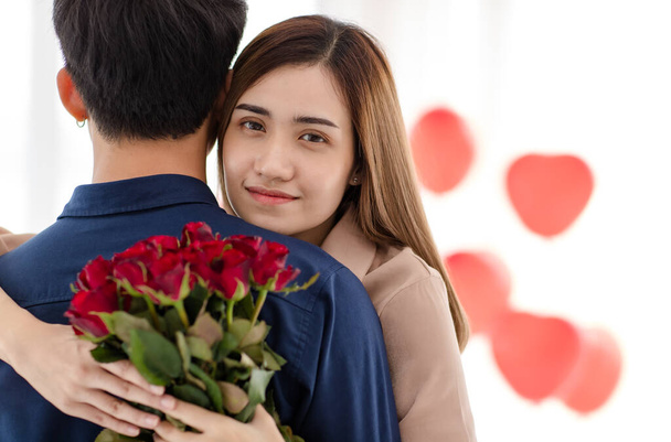 Asiatische Frau mit Blumenstrauß umarmt Mann und blickt während der Valentinstagsfeier in die Kamera. Liebe und Beziehung von Teenie-Liebhabern. - Foto, Bild