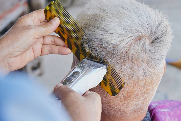 Borbély vagy fodrász használata Clipper és fésű vágott vissza a haj az öreg ember otthon borbély bolt - Fotó, kép