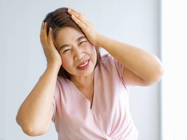 Femme âgée utilisant les mains pour attraper et tenir sa tête avec douleur et souffrir de maux de tête déformés avec une maladie cérébrovasculaire ou un accident vasculaire cérébral. - Photo, image
