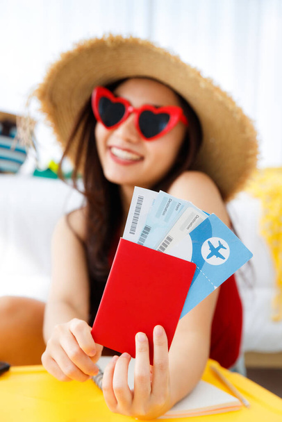 Mladý šťastný a vzrušený asijské žena cestovatel se připravuje na letní dovolenou výlet s její jasně žlutý kufr nosí ve tvaru srdce sluneční brýle drží pas letadlo. - Fotografie, Obrázek