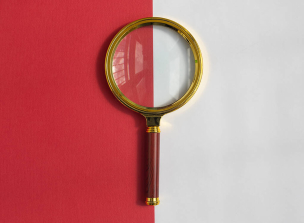 Golden magnifying glass over red and white background. Search tool. SEO concept - Fotografie, Obrázek