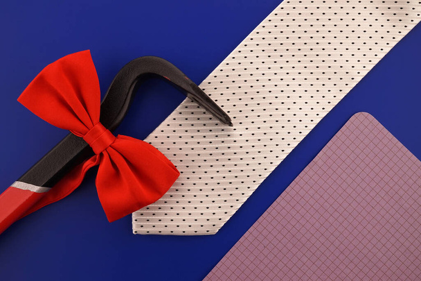 Still life with fashion accessories including an elegant necktie and red bow tie, crowbar and blank sheet of notepaper with copy space over a blue background - Foto, Imagen