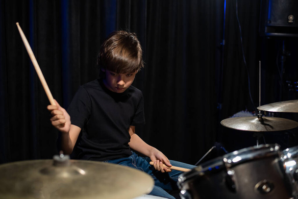 The boy learns to play the drums in the studio on a black background. Music school student - Φωτογραφία, εικόνα