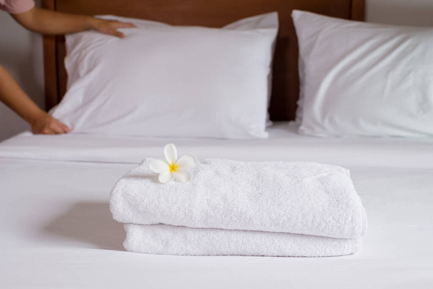 Una cameriera dell'hotel impilava asciugamani sul letto e metteva fiori sugli asciugamani in una camera d'albergo. - Foto, immagini