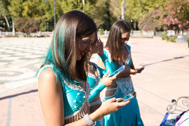 Tres hermosas bailarinas del vientre adultas están revisando sus teléfonos móviles. Están mirando mensajes, correos electrónicos y fotos. Concepto de tecnología móvil - Foto, imagen