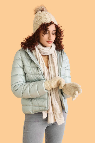 Woman in knitted hat putting on gloves on color background - Фото, зображення
