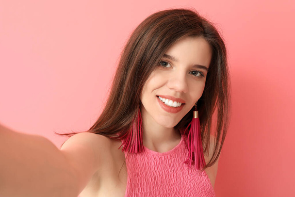 Stijlvolle jonge vrouw het nemen van selfie op kleur achtergrond - Foto, afbeelding