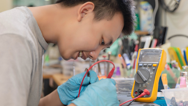 Phone repair concept a young electrical technician using an ammeter measuring the current in a circuit of an electronic device. - 写真・画像