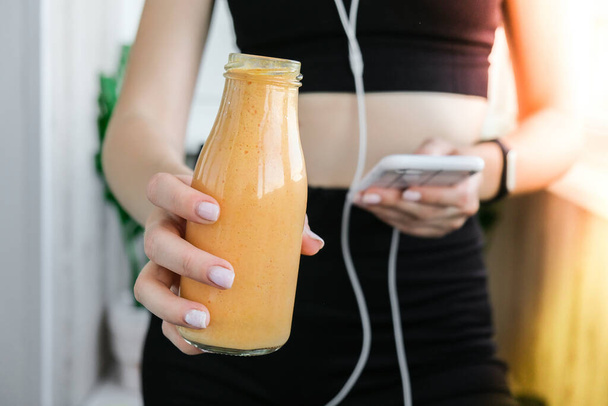 Young millenial woman checking smartphone drinking vegan smoothie drink detox. Woman doing yoga exercises at home. Online tuition Clean eating, weight loss, healthy dieting food concept. Stay healthy. Wellness - Fotó, kép