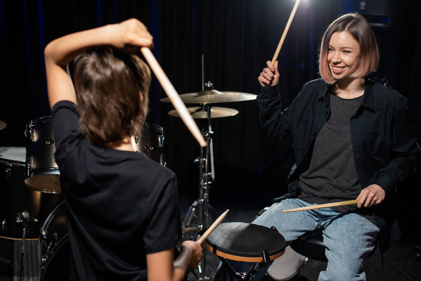Young caucasian woman teaches a boy to play the drums in the studio on a black background. Music school student - Zdjęcie, obraz