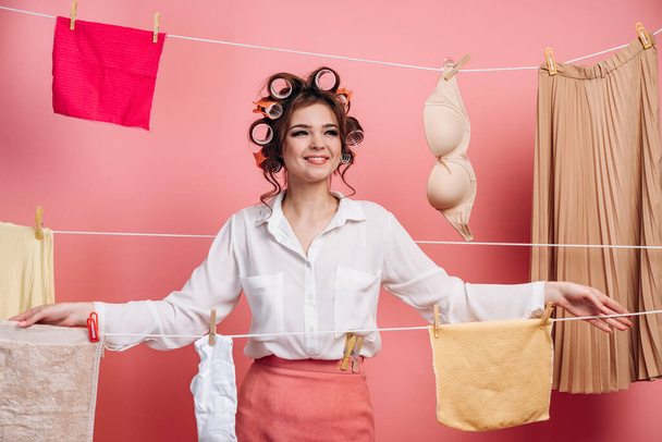 Cute, young housewife on a background of ropes with clothes on a pink background. A smiling woman is happy that she did all the work. - Photo, Image