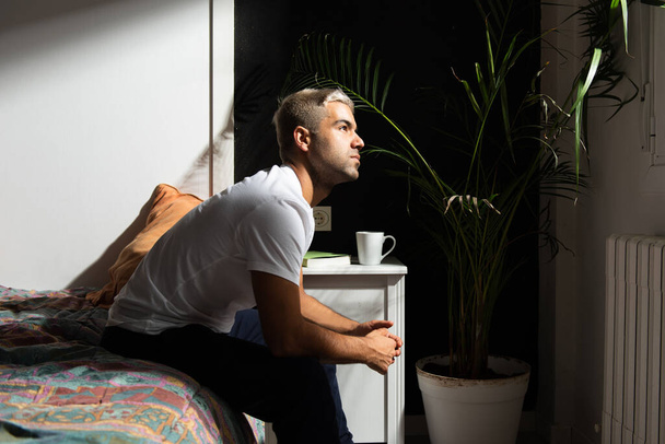 Homme hispanique réfléchi assis sur son lit en pensant à ses problèmes. Stress, anxiété, dépression et santé mentale concept. - Photo, image
