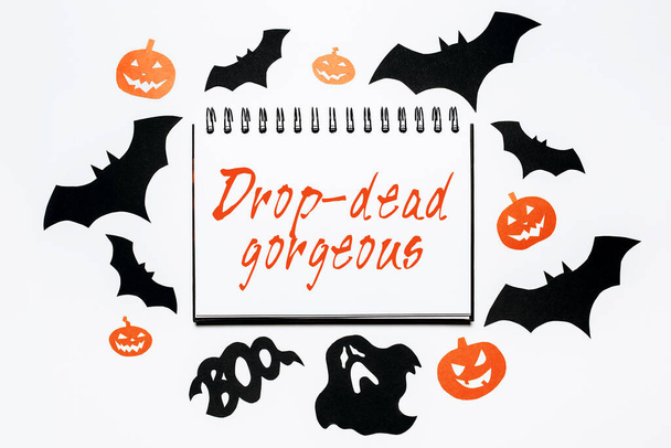 Happy halloween holiday concept. Notepad with text Drop-dead gorgeous on white background with bats, pumpkins and ghosts - Zdjęcie, obraz