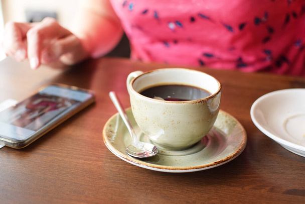 Woman with smartphone drinks coffee in a cafe. A cup of coffee on a table in a cafe.  - Фото, зображення