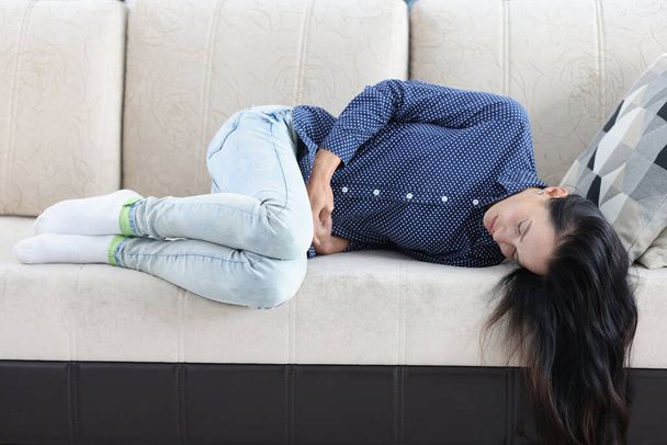 Tired woman lies on couch with abdominal pain - Foto, imagen