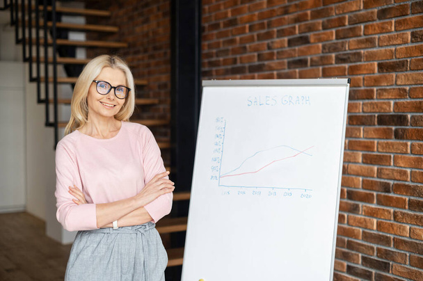 High-skilled business coach with arms crossed stands near whiteboard with graphs - Photo, Image