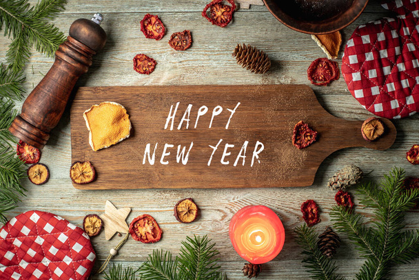 Coniferous branches, festive and kitchen accessories and a brown cutting board with inscription Happy New Year on a wooden background. Top view. - Foto, imagen