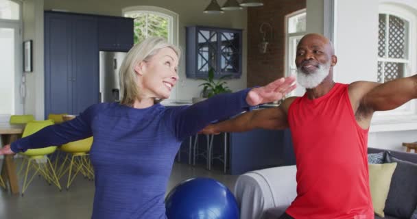 Mixed race senior couple performing stretching exercise together at home. retirement and active senior lifestyle concept - Metraje, vídeo